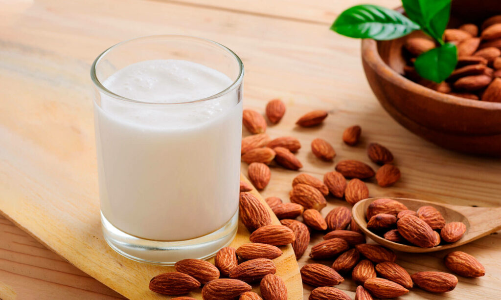 image representing a glass full of almond milk aongside almonds