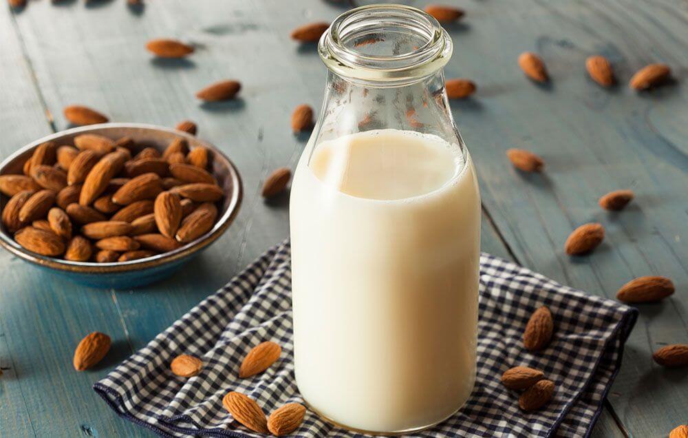 image representing a bottle full of almond milk with almonds aside