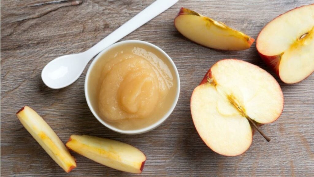 image representing a bowl full of apple sauce alongside some apple slices