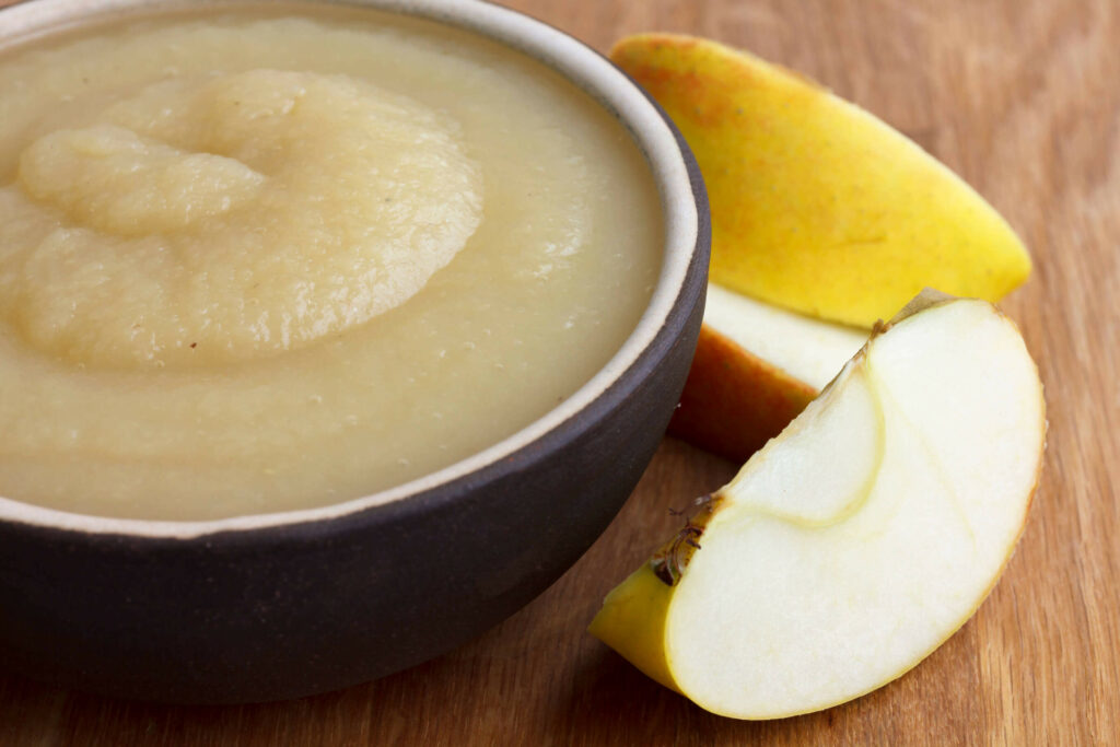 an image representing a bowl full of applesauce alongside apple slices