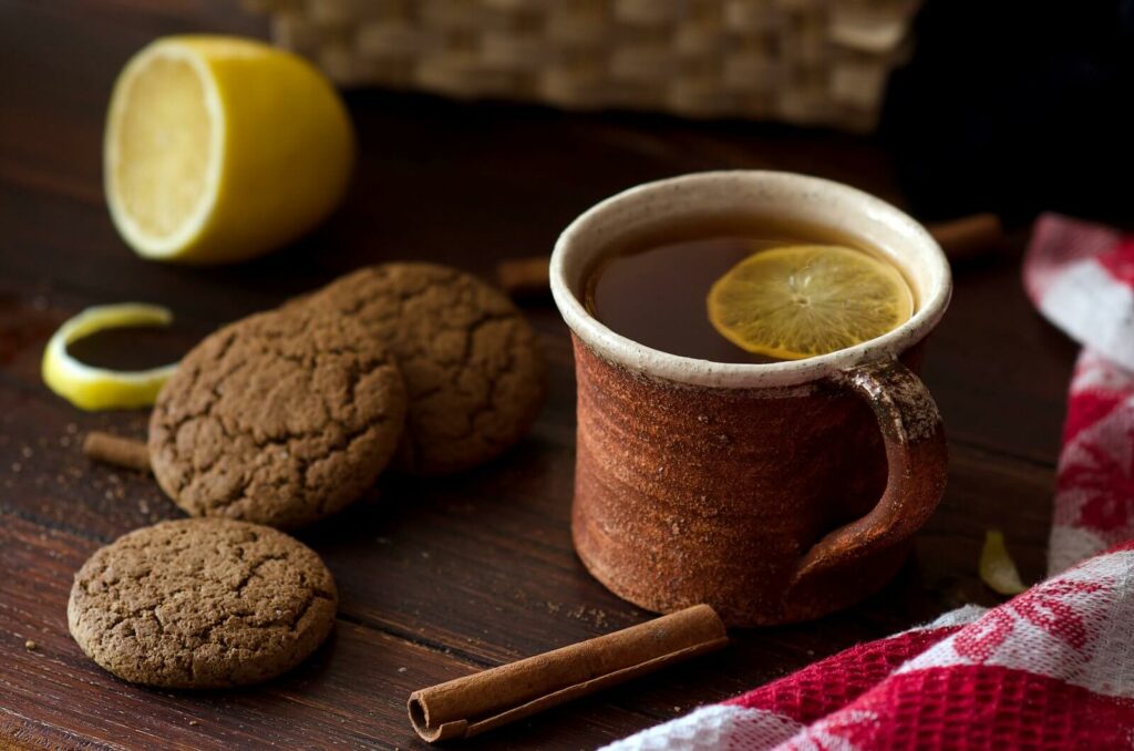 image representing a cup of cinnamon tea and a lemon slice alongside cinnamon sticks and cookies