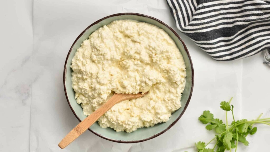 image representing a bowl full of cottage cheese alongside some corriander leaves