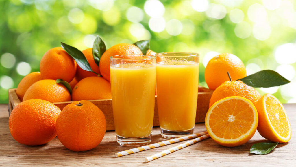 image representing a pair of orange juice glasses alongside some oranges