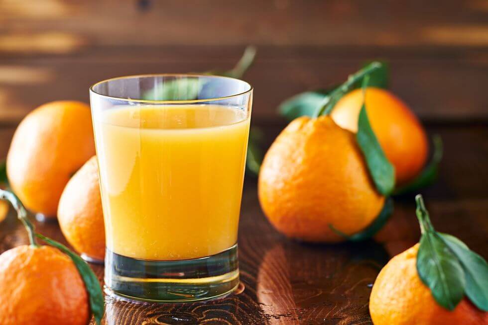 image representing a glass full of orange juice alongside some oranges
