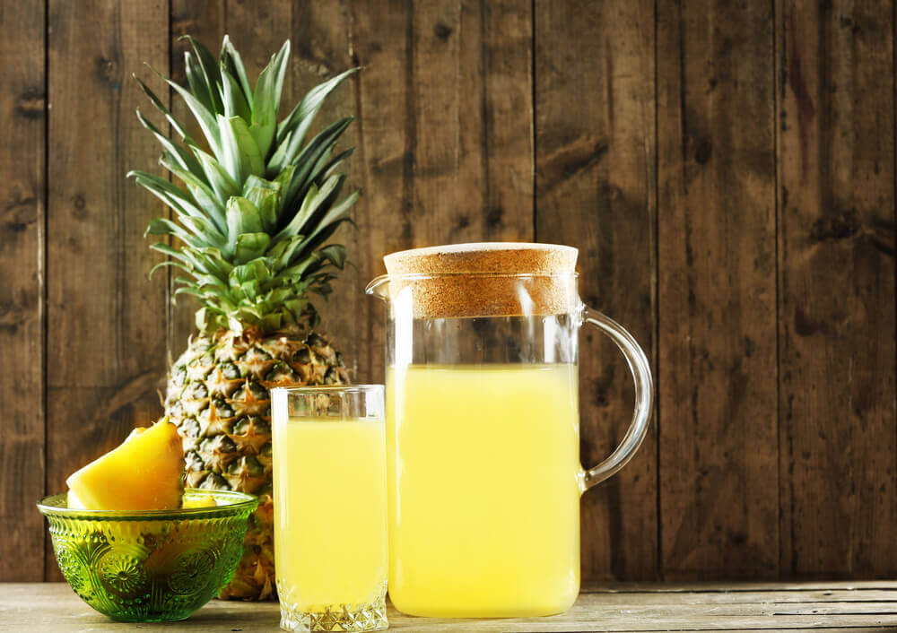 image representing a jar and a glass full of pineapple juice alongside a pineapple